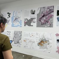 A student reads posters from classmates with maps and text pinned up on a white wall.