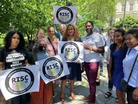 A multicultural group of varied ages poses for a photo with RISC signs 