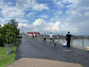 A black paved path runs along the waterfront. A handful of people fish over the metal railing.
