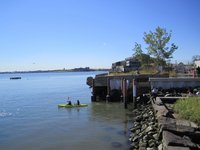 Two people canoeing in the East River after pushing off from the rocky shore of Hunts Point landing