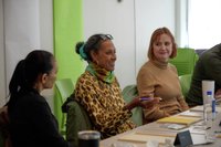 Group of three at a table, one is addressing the larger group.