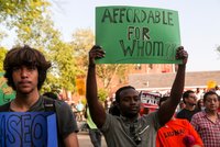 Person in a crowd of demonstrators holding a sign above their head that reads "Affordable for Whom??"