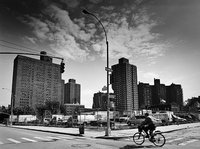 Man cycles by the vacant and fenced in SPURA site containing large trucks and vans. Large high rise buildings are seen in the background