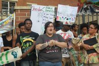 A group of young people gather at a rally to remove the Sheridan Expressway. One woman speaks while others hold signs reading "Sheridan < Public benefits: Safer streets, new space, parks, affordable housing"