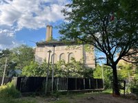 Photo of an older neoclassical style building, a fence in front, and a large tree. 
