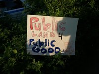 Hand made poster placed in some greenery reads "Public Land 4 Public Good: Don't Give Away Our Land"