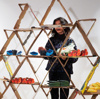 A rendering shows a triangular shelving system constructed with empty produce boxes holding various fruits and vegetables 