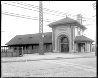 Historic, black and white image of subway station; large arched entrance and tile roof.