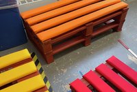 Orange, red and yellow cushions on top of benches made from wooden pallets. 
