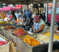 Serving trays and chafing dishes heaped with food at a busy outdoor food market.