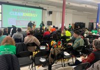 Large, diverse group of people seated in black folding chairs watching a presentation on the Manhattan Clean Energy Survey.